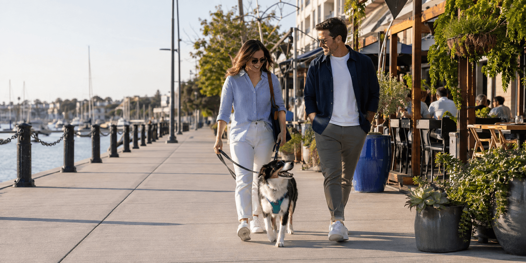 Two people walking their dog along a waterfront restaurant district